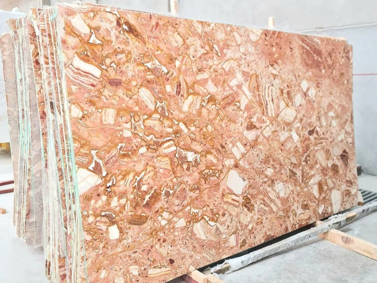 polished Ceppo Rosa marble slabs stacked in warehouse with dusty rose brown matrix and cream ivory brecciated fragments